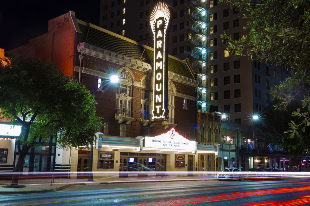 The illuminated Paramount Theatre in Austin, TX set against the blurry traffic of the city and the surrounding dark night. | US Ghost Adventures