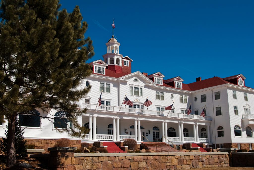 An angled view of the Stanley Hotel in Estes Park Colorado with a tree in the foreground.