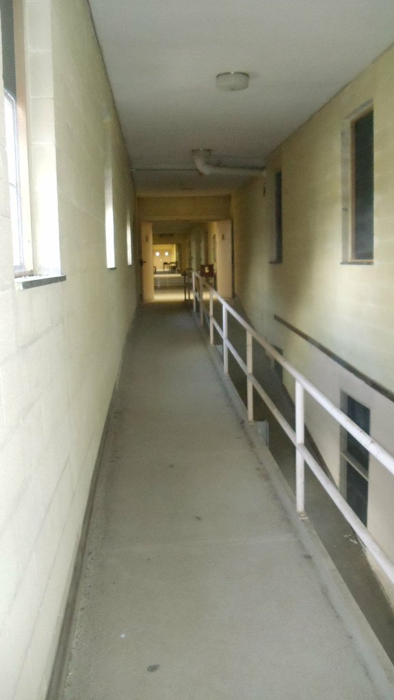 photo shows a poorly lit hallway with a railing on one side, leading to an open door.