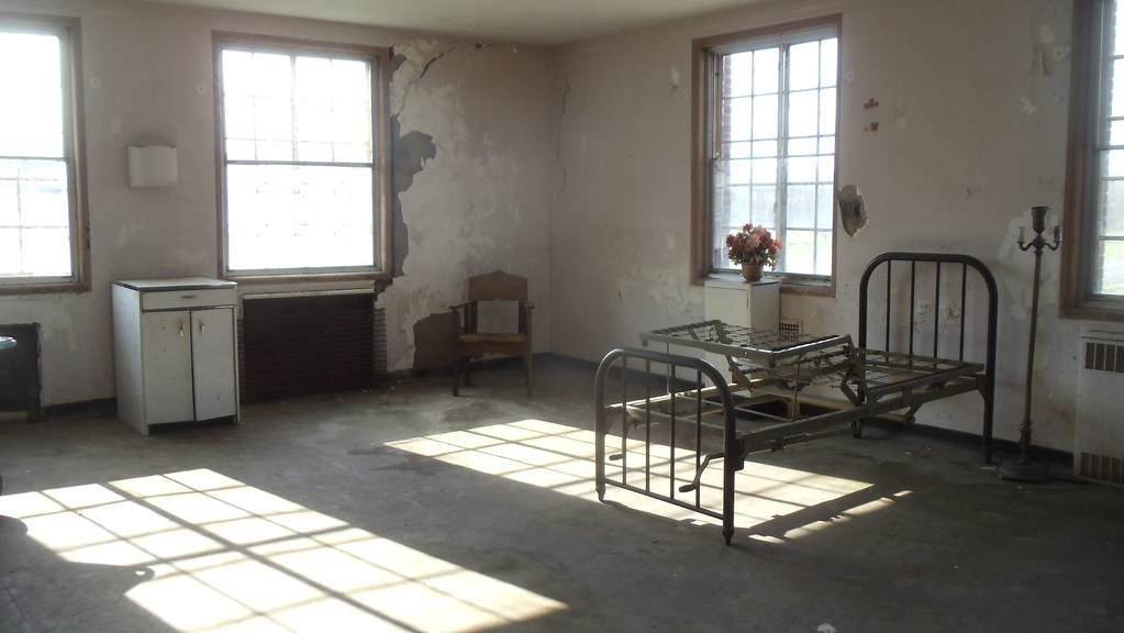 Photo shows an old patient room, with an abandoned bed and peeling paint
