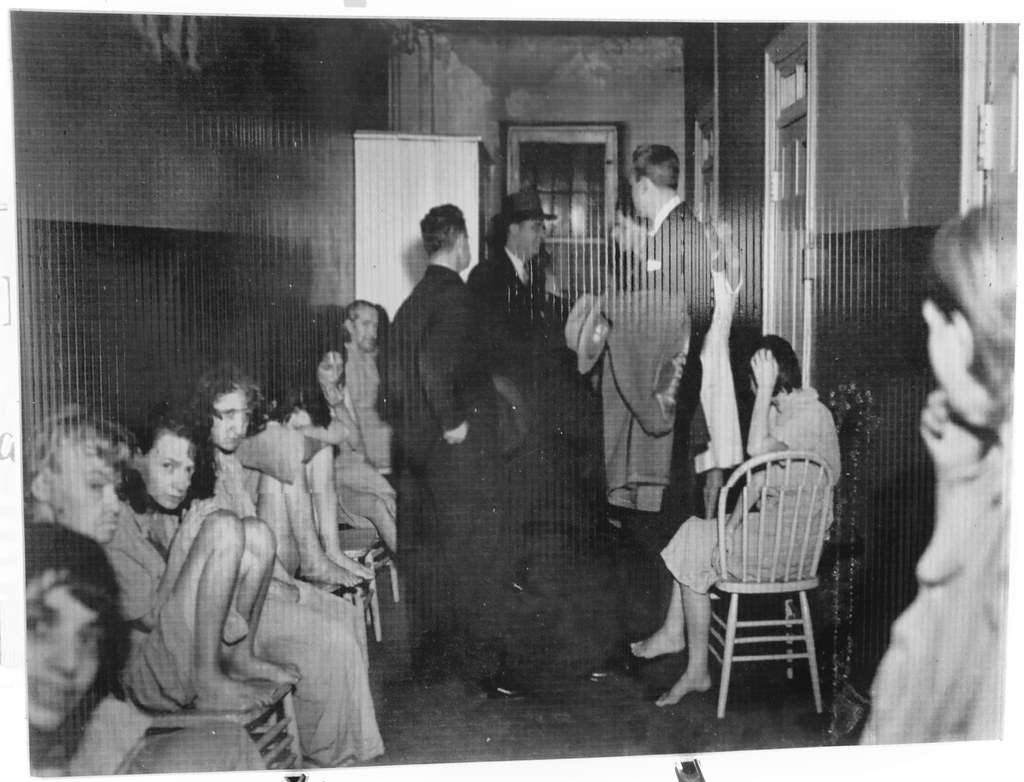 photo shows about ten patients sitting in a small room with a couple of men in suits talking to a doctor