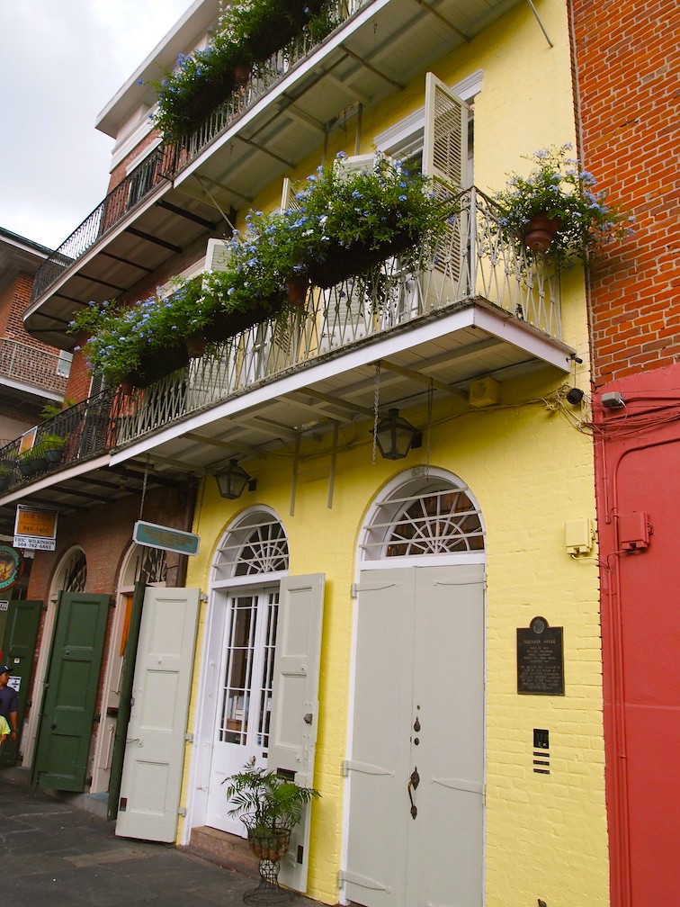 photo shows a colorful row of houses in the historic french quarter of new orleans. plants hang over the balconies.