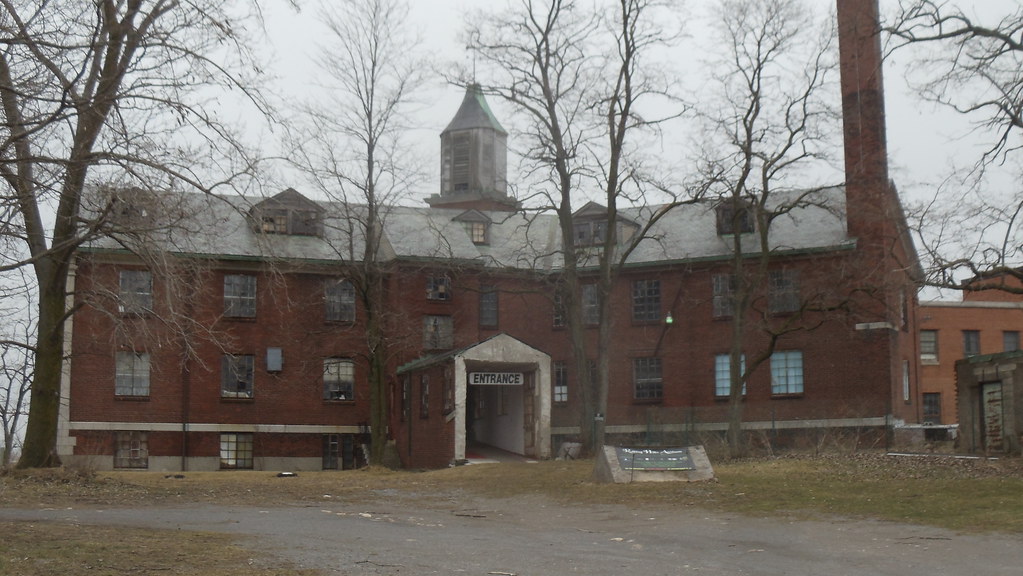 photo shows the facade of the rolling hills asylum. it has red brick with five trees surrounding the front.