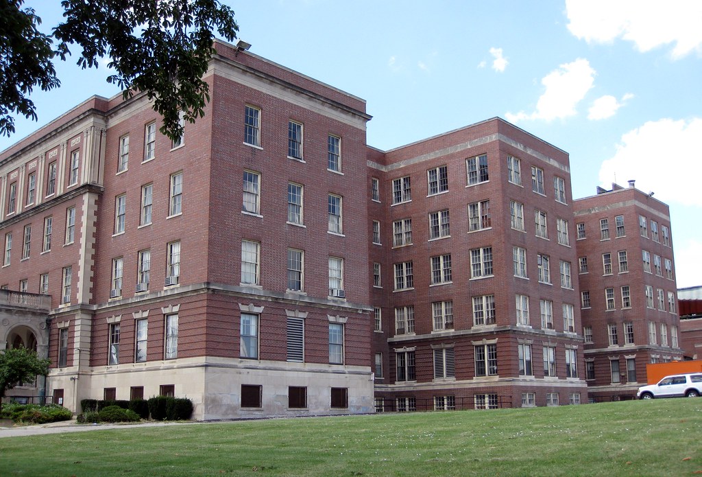 photo shows a large red brick building with many windows overlooking a green grassy area.