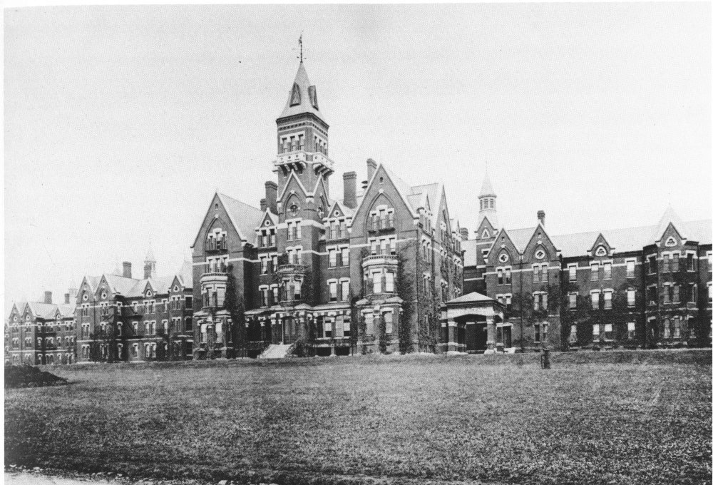 photo shows a castle-like structure over a grassy field, there are lots of windows, brick, doors, and towers. 