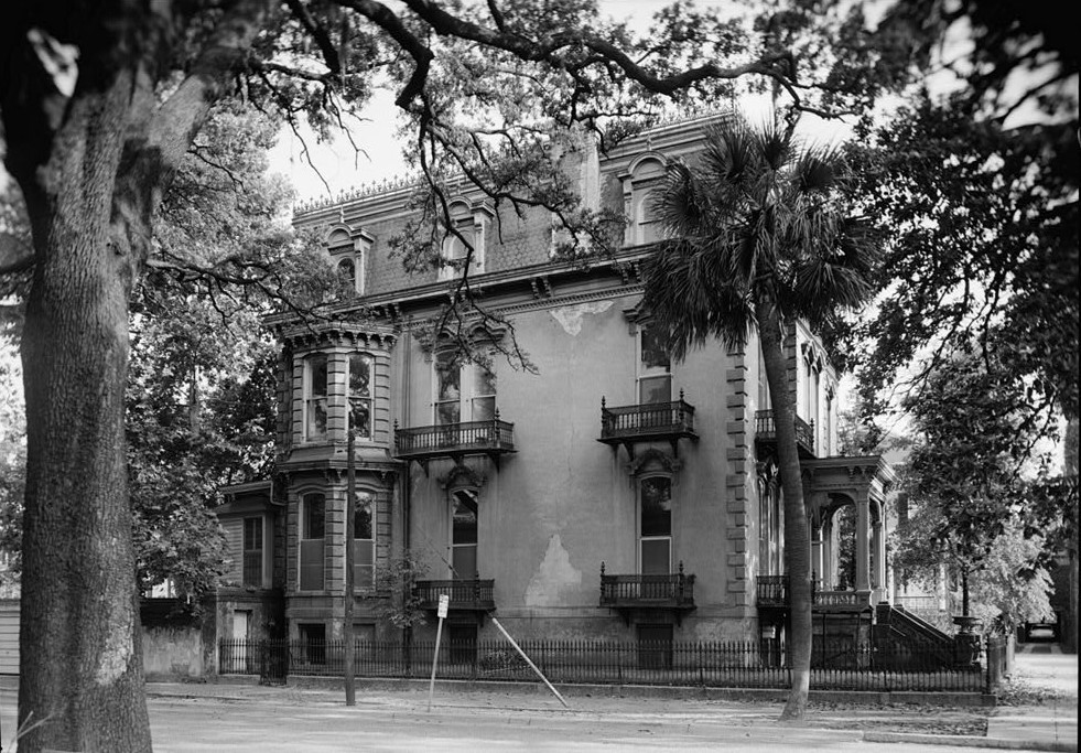 photo shows a black and white image of the hamilton turner home from the street. black iron balconies are on the side of the house. 