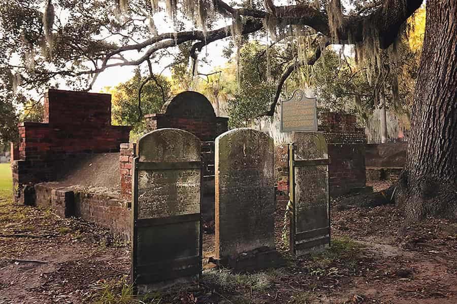 photo shows a few weathered headstones underneath a mossy oak tree