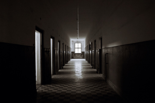 photo shows a dark hospital hallway with light only coming in from a window at the end of the hall