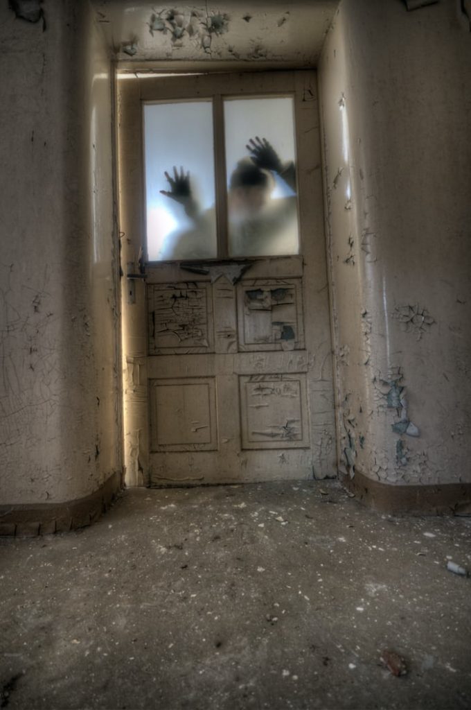 photo shows a shadow with its hands against a broken door with frosted glass. he seems to be peeking in 