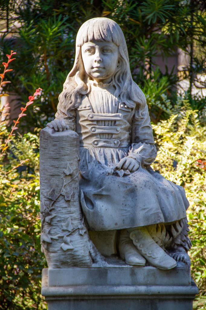 photo shows the stone statue of gracie watson. It's a little girl sitting with her hand on a log
