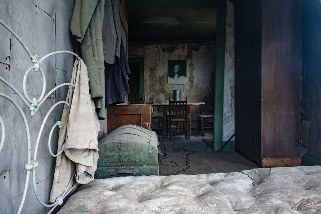 photo shows an old bed and frame with dusty belongings of the person who once lived there.