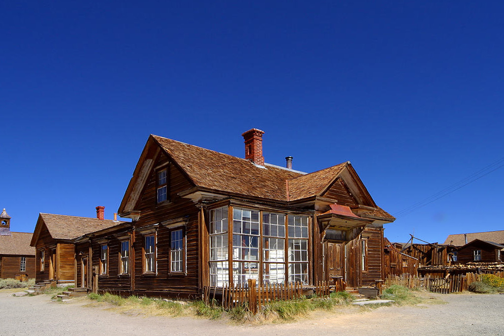 photo shows an old wooden home, windows in tact with a sunny and clear sky as the backdrop.