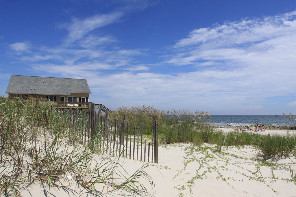 photo shows a small sand dune at pawleys island with the ocean front in the background. a small wooden fence is in the foreground