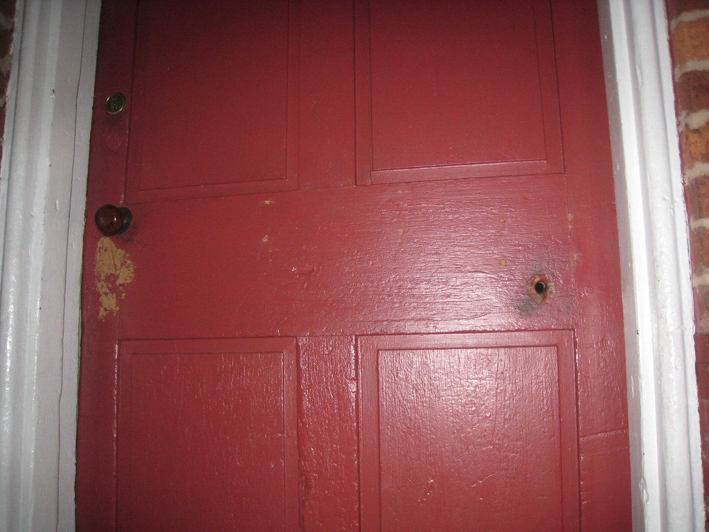photo shows a red wooden door with a bullet hole in it