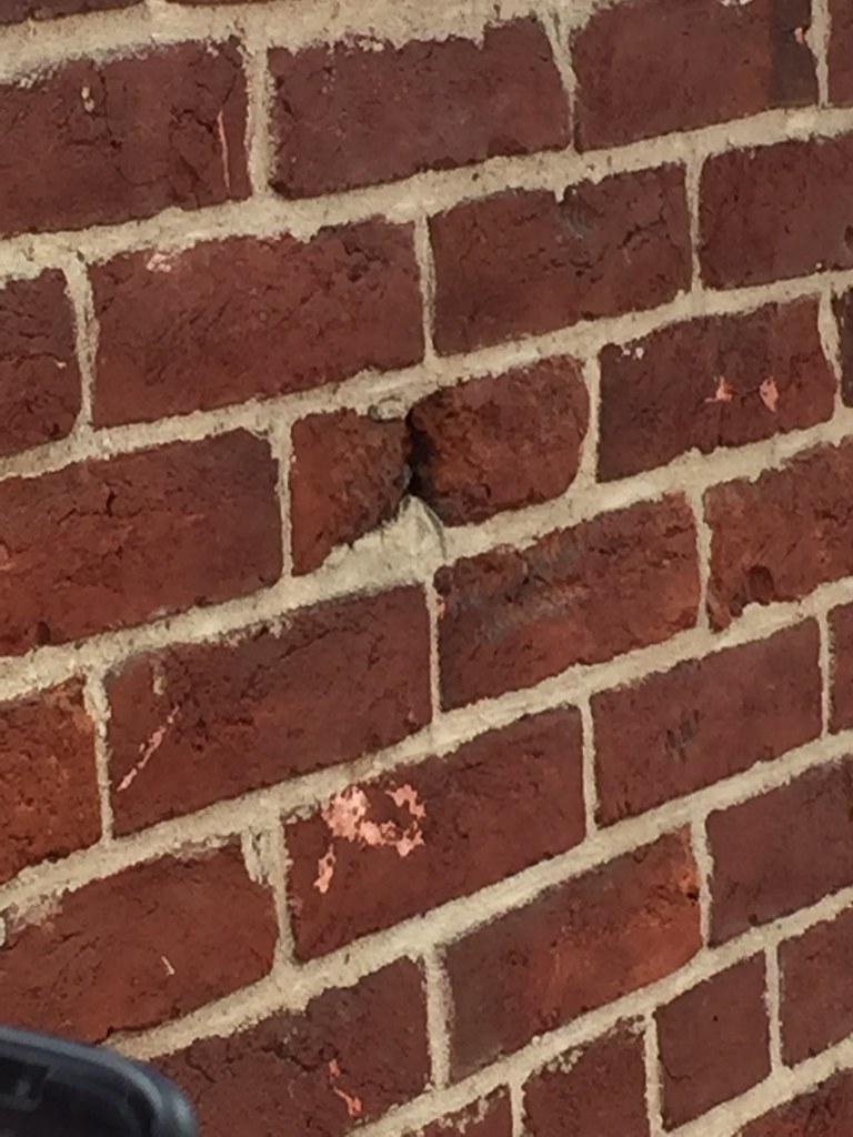 photo shows a brick wall with a bullet hole in it 