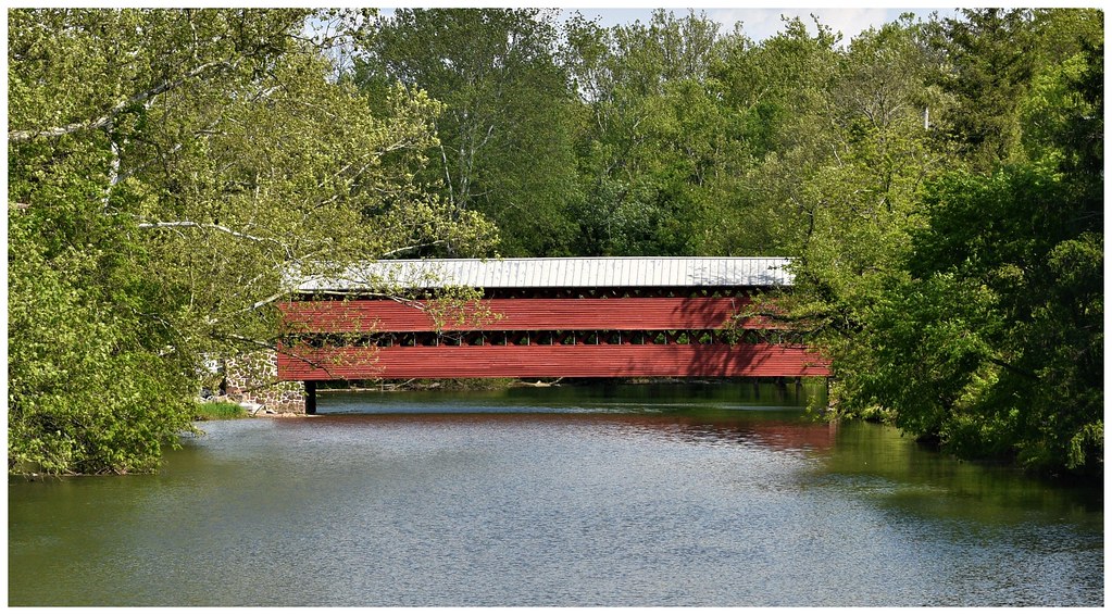 photo shows a red covered bridge sitting above a calm river