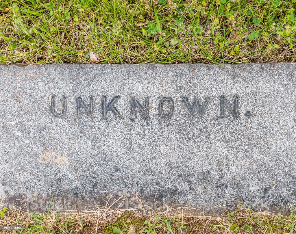 Simple grey stone grave marker with the word UNKNOWN engraved on it. Surrounded by green grass.