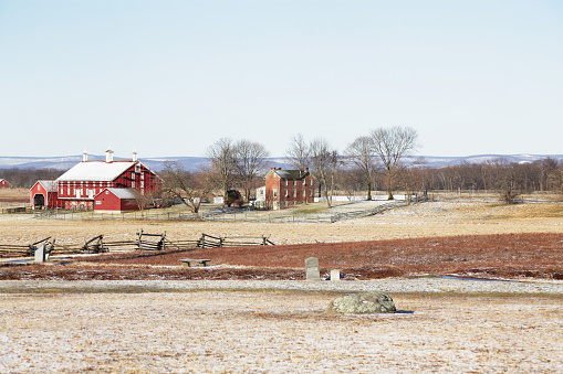 A preserved American Civil War era farm house and farm outbuildings located at the edge of the Gettysburg battlefield in late winter. The big barn on the left is surrounded with construction scaffolding. Similar structures are preserved all around the Gettysburg National Military Park commemorating the people and way of life during the Civil War era. Various monuments and memorials scattered in the foreground are located where key events occurred during the bloody battle fought here by Union and Confederate forces between July 1st and July 3rd, 1863.