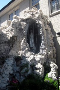 A plaster casing shaped like rocks enshrines a statue of a saint behind metal bars