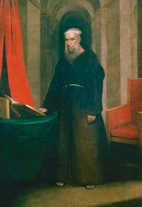 A Spanish priest, bald with large white beard in black priest robe