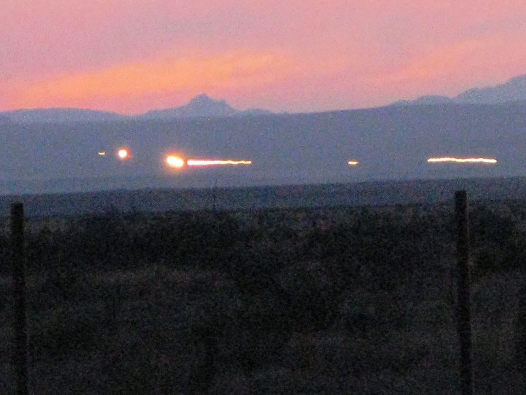 Streaks of Light Cast Upon A Sunset Backdrop. Mountains in the Background, Desert Bush Below