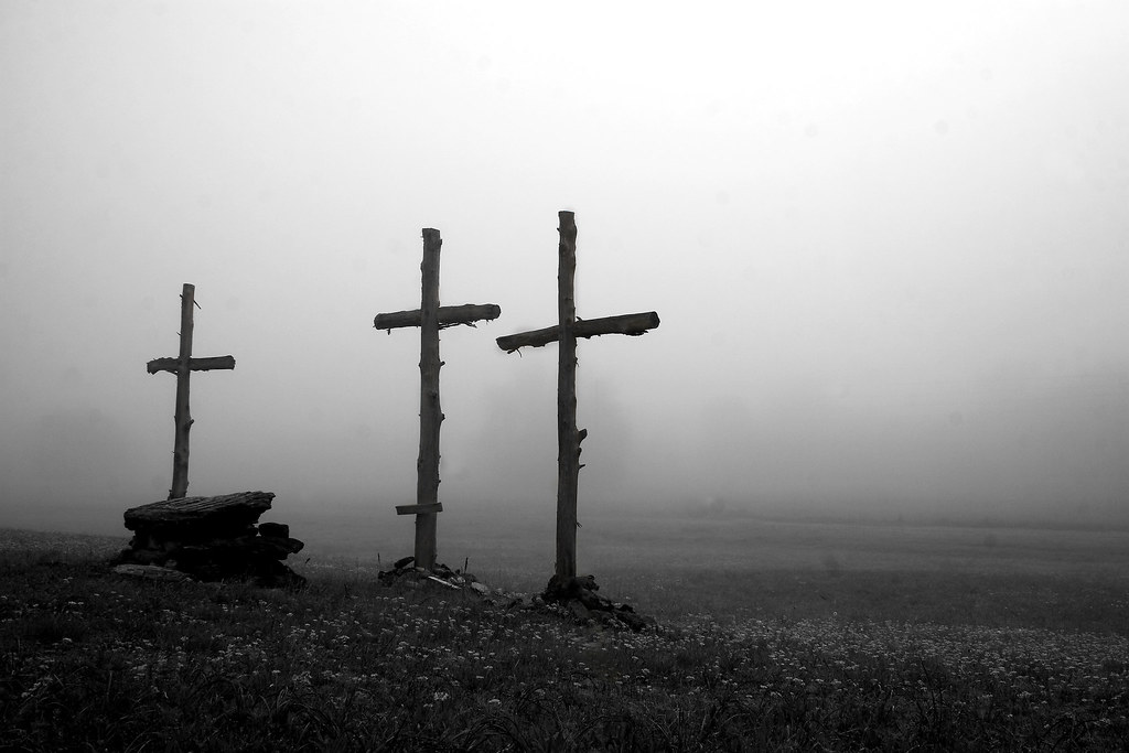 Three crosses stand in an empty, misty field. In Black and white