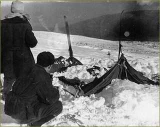 Dyatlov Pass. Black and white photo of a torn apart tent in the snow with two people looking on