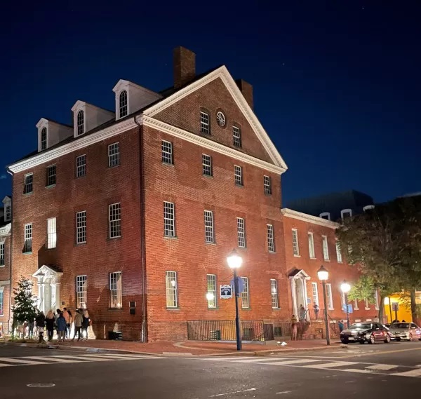 Colonial styled multi level brick house at night. Building is on a corner with cross walk and street lights. Gadsby's Tavern.