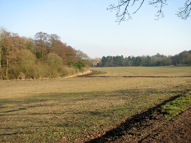 A large green/brown field. A red brick house in the distance