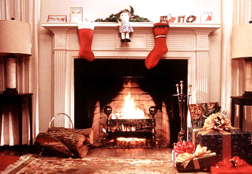 Christmas. Photograph of a yule log burning in a hearth. Two stockings hang overhead. 