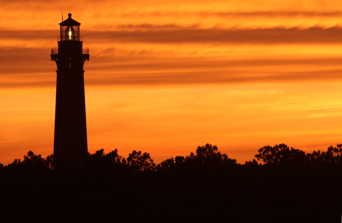 A lighthouse is seen in front of a beautiful Outer Banks sunset