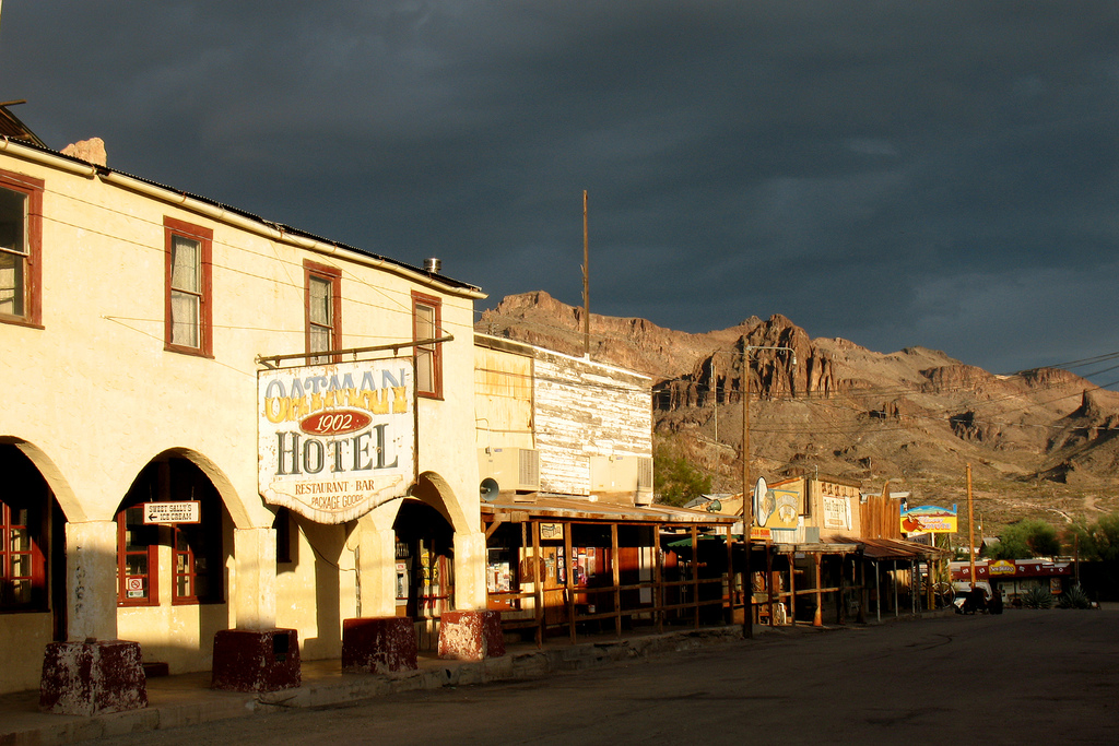 Brick hotel backdropped by a small hill and cloudy skies. Sign in front readys Oatman Hotel. 1902