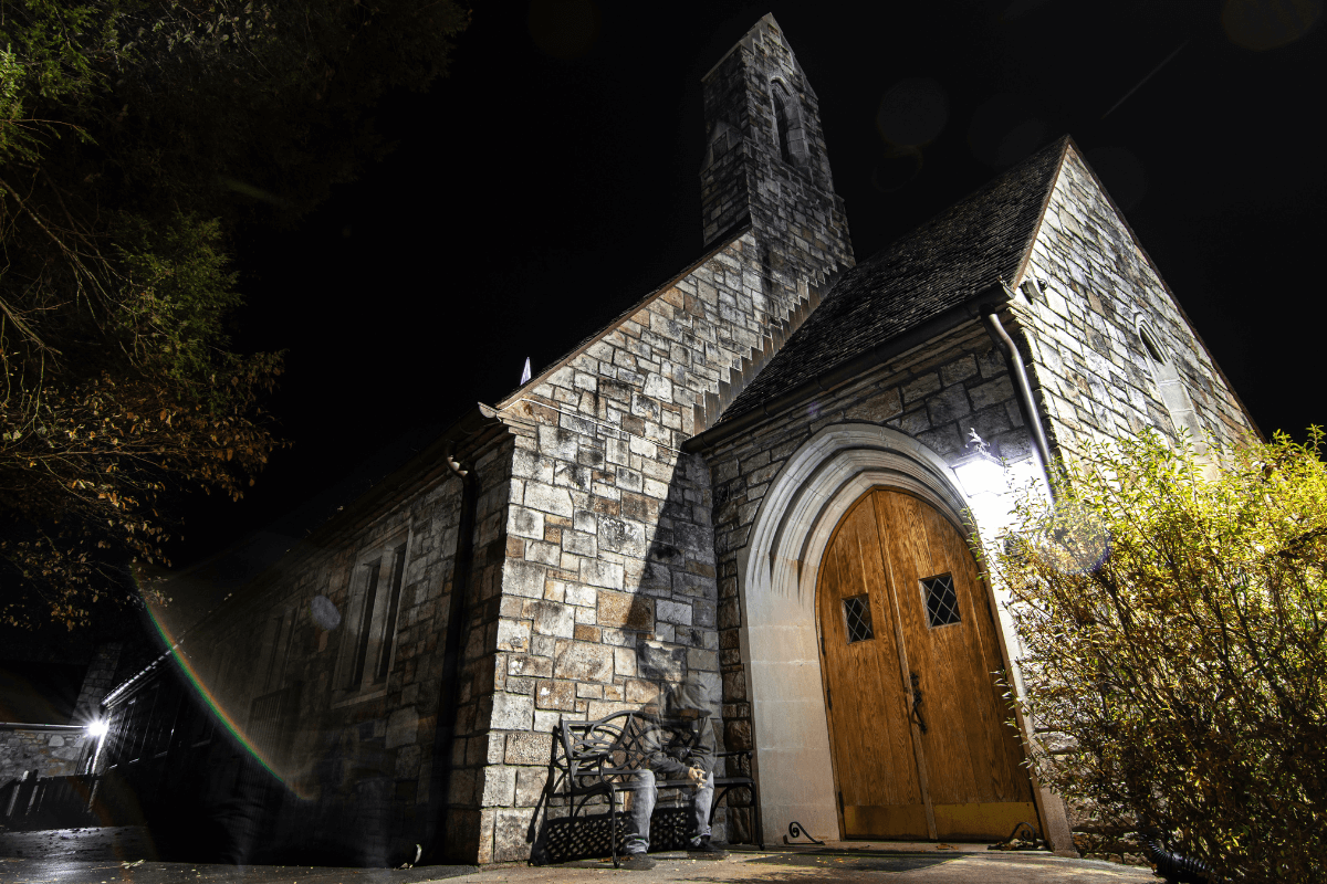 Night photo of beautiful dark sky with illuminated clouds. A historic stone First United Methodist Church in foreground with brown wooden door and foliage.