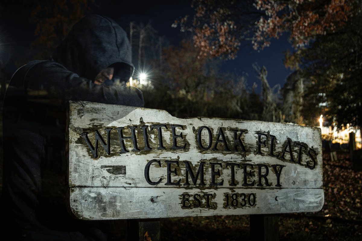 weathered wooden white sign reading White Oak Flats Cemetery EST. 1830 at night